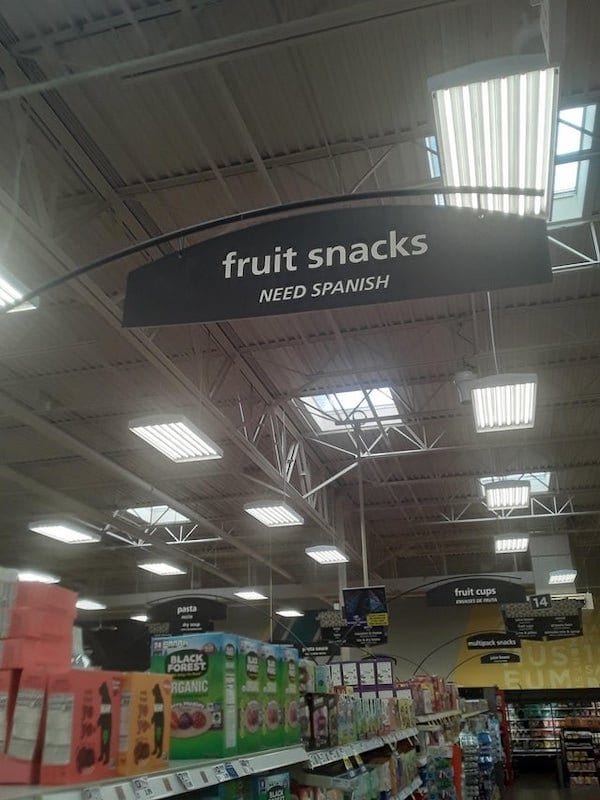 Grocery aisle sign reads 'fruit snacks' and then underneath 'need Spanish'.